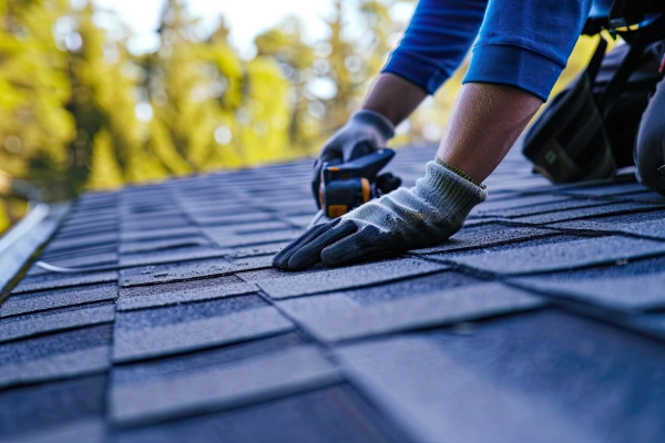 Roofing contractor installing asphalt shingles with proper technique and safety equipment