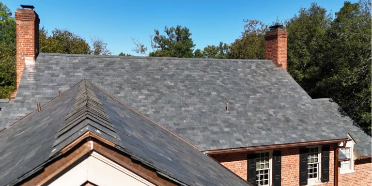 Slate roof with copper flashing on a historic brick home with two chimneys and mature trees in the background